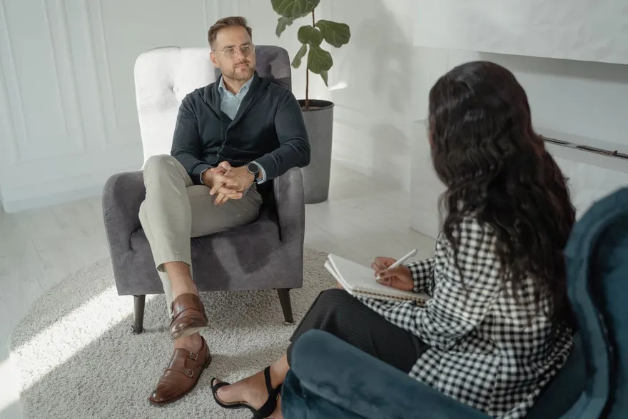 A man sitting in an armchair talking with a counsellor, who is taking notes
