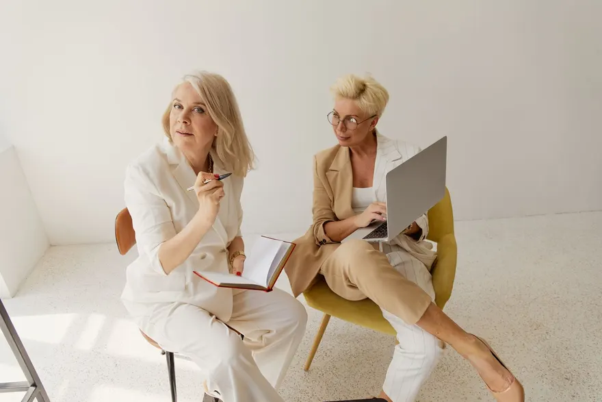 Two experienced clinicians reviewing notes together, one with a notebook and one with a laptop