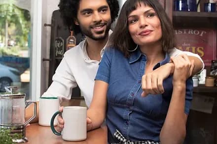 A couple sitting together over coffee, one leaning into the other