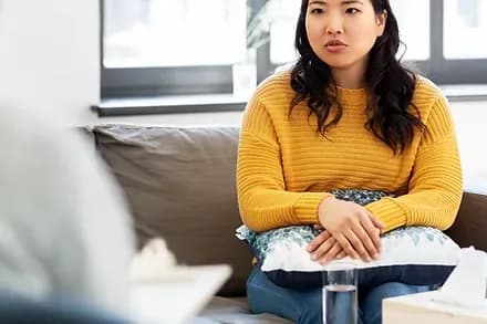 A young woman sitting quietly on a couch in a counselling room, looking away