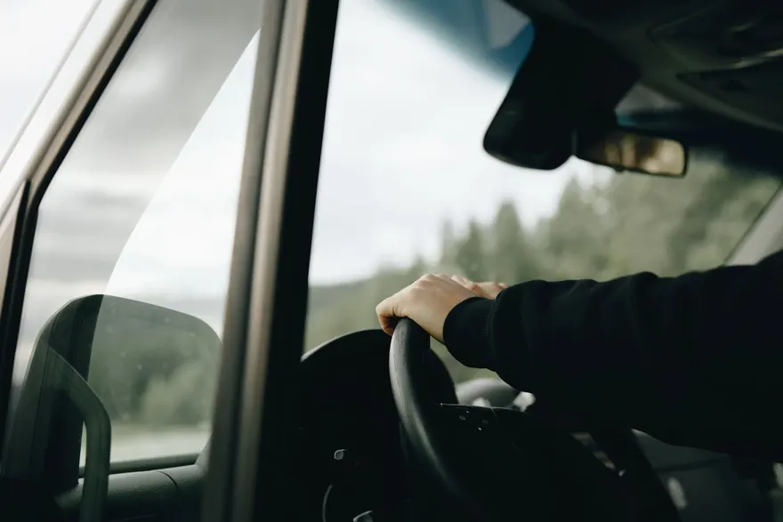 A driver’s hand on the steering wheel, with trees visible through the windscreen