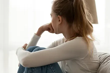 A woman sitting with her knees drawn up, looking out of a window