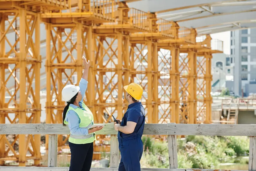 Two workers in hard hats and safety gear talking on a construction site